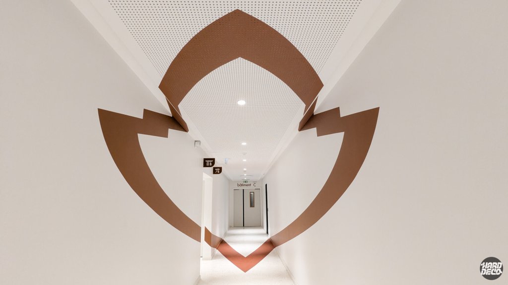 Anamorphose couloir entreprise Warner, logo écusson brun-rouille sur murs plafond et sol, point de fuite