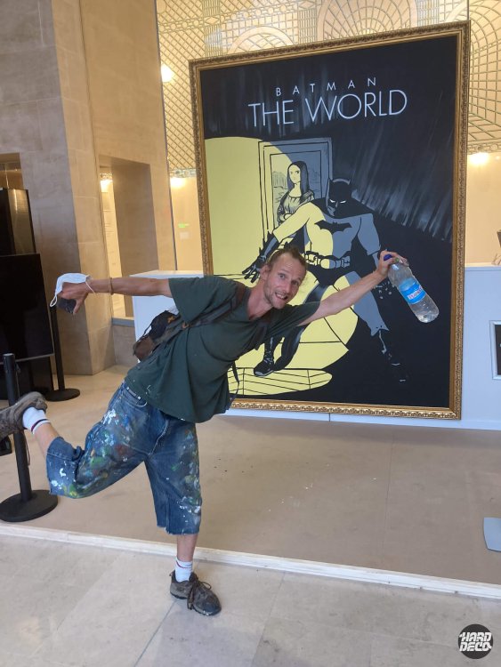 Artiste Samy posant devant la toile encadrée Batman The World terminée dans le hall du Louvre