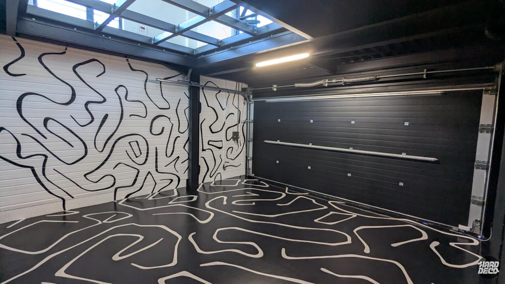 Angle du garage avec portes sectionnelles peintes en motifs abstraits et sol résiné noir lignes blanches