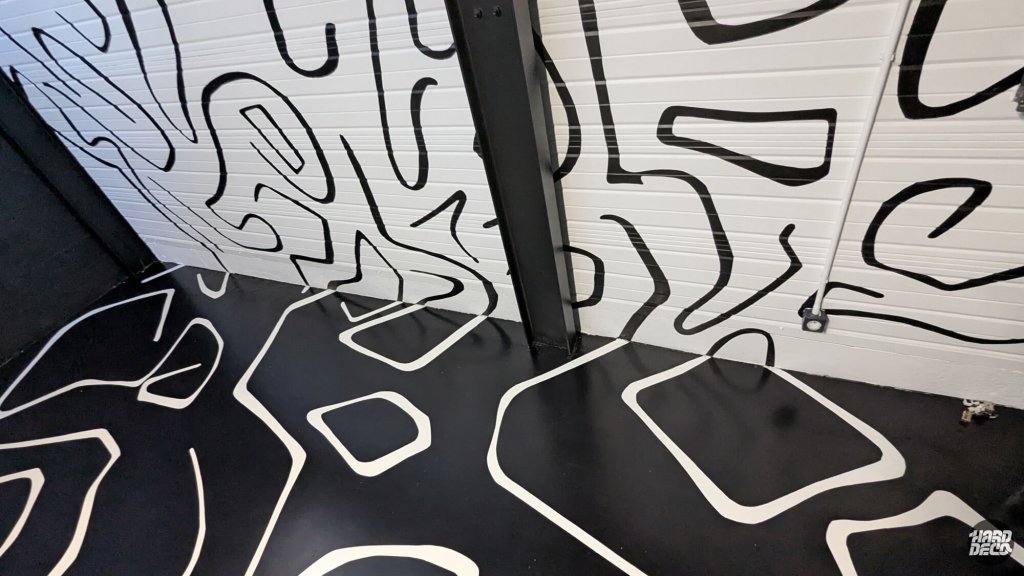 Détail de la continuité du tracé abstrait entre les portes sectionnelles et le sol résiné noir du garage