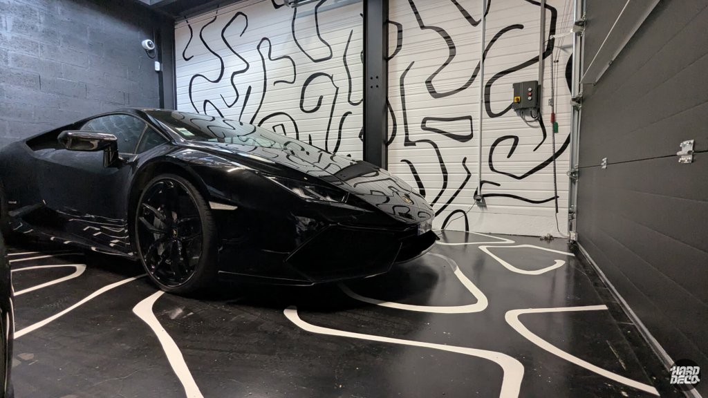 Lamborghini noire garée devant la fresque abstraite noir et blanc sur portes de garage, reflets sur carrosserie
