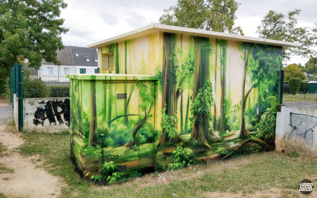 Vue d'ensemble du transformateur EDF peint en forêt, local technique et armoire couverts de végétation aérosol