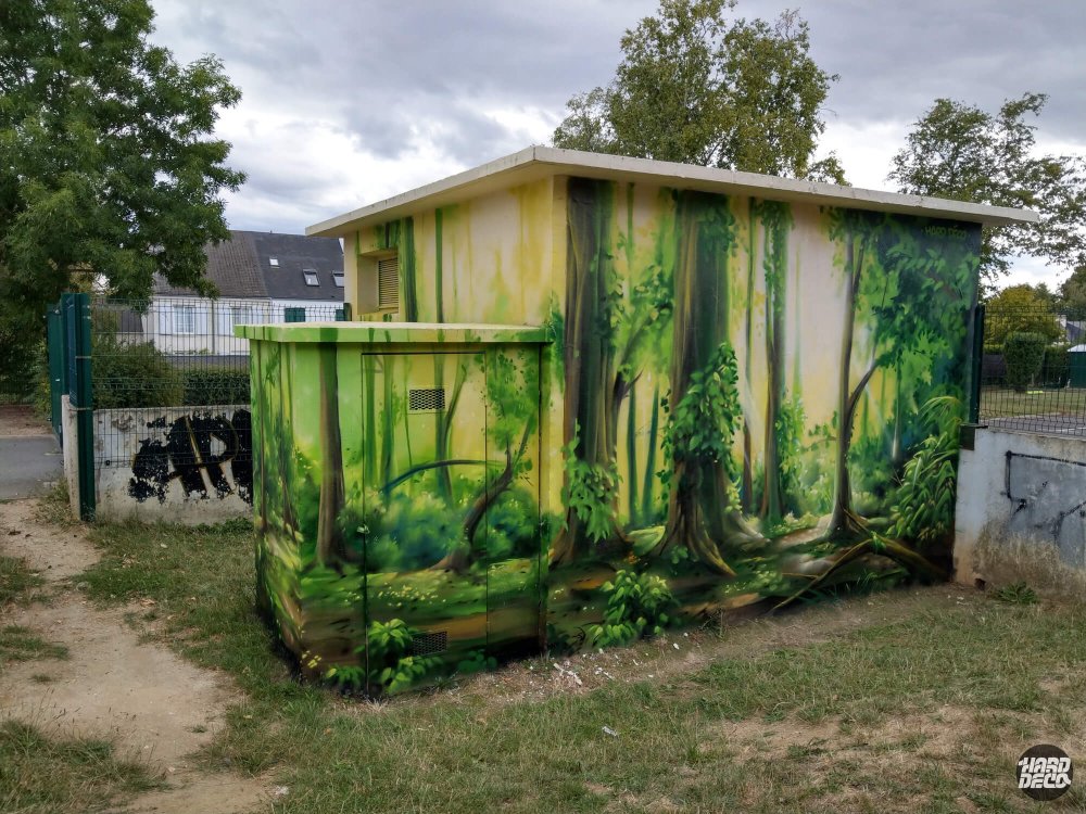 Transformateur EDF décoré d'une fresque forêt verte à l'aérosol, vue d'ensemble depuis terrain de sport
