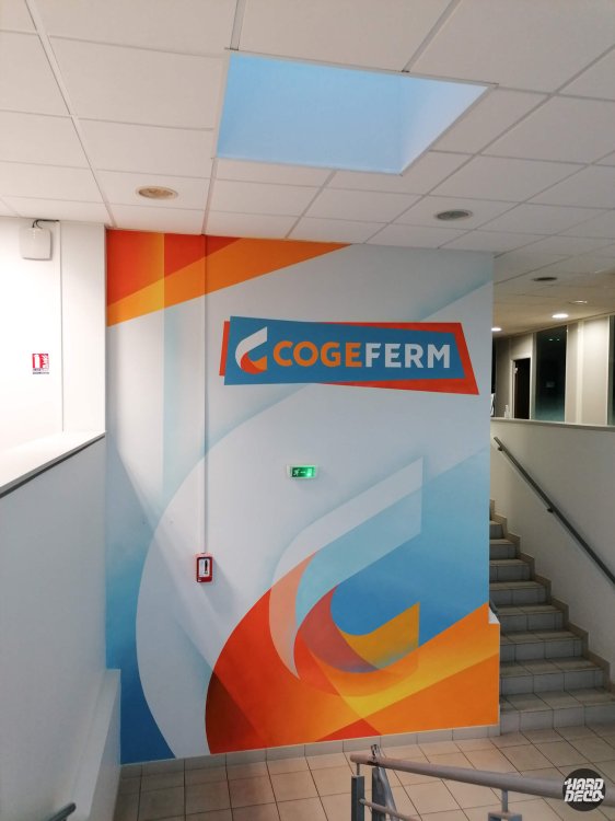 Toile aérosol avec logo Cogeferm sur fond de formes abstraites orange et bleu dans cage d'escalier