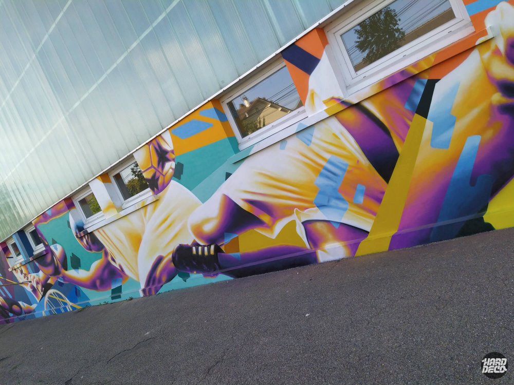 Gros plan fresque aérosol gymnase Pontault-Combault, sportif en mouvement jaune et violet, détail façade