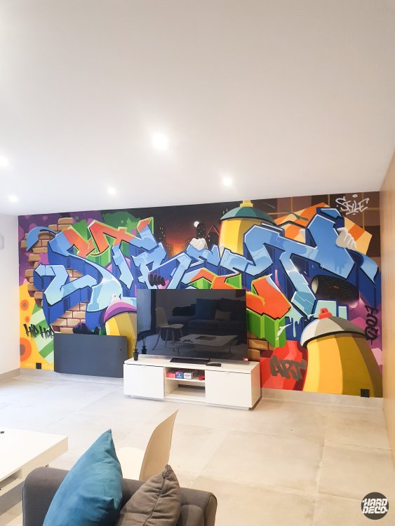 Fresque graffiti hip-hop salon, vue avec canapé au premier plan, détail bombe aérosol géante jaune à droite