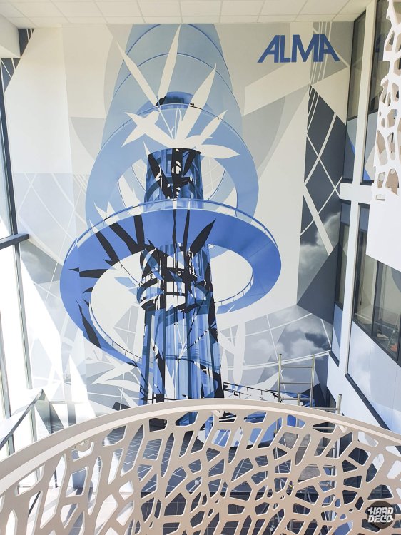Détail haut de la fresque ALMA : ascenseur stylisé en bleu cobalt, anneaux géométriques et logo de marque