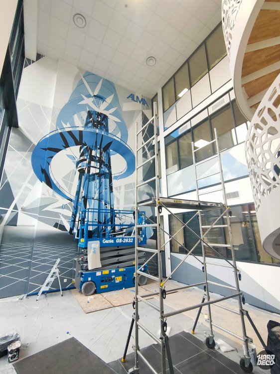 Fresque murale ALMA en cours de peinture, nacelle ciseaux au pied du mur, composition géométrique abstraite