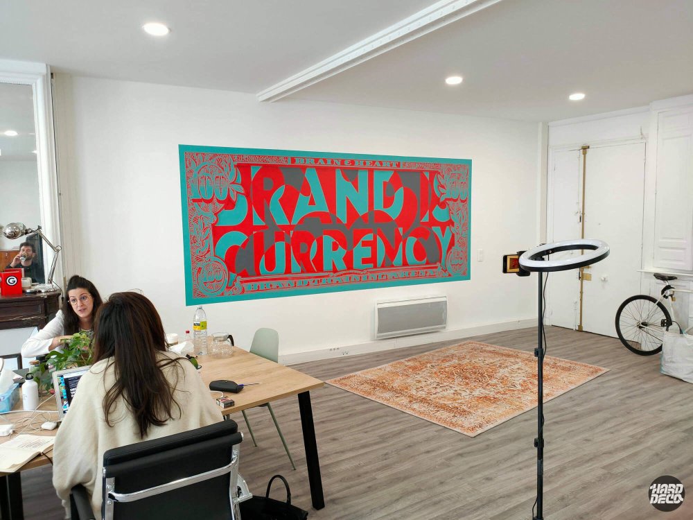 Open space agence Brain & Heart Paris avec toile murale billet dollar détourné rouge turquoise