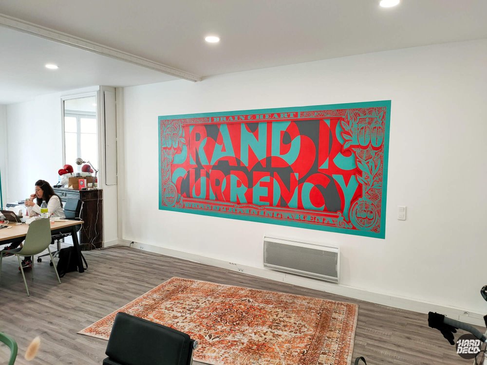 Fresque murale billet de dollar détourné avec slogan Brand is Currency dans bureaux parisiens