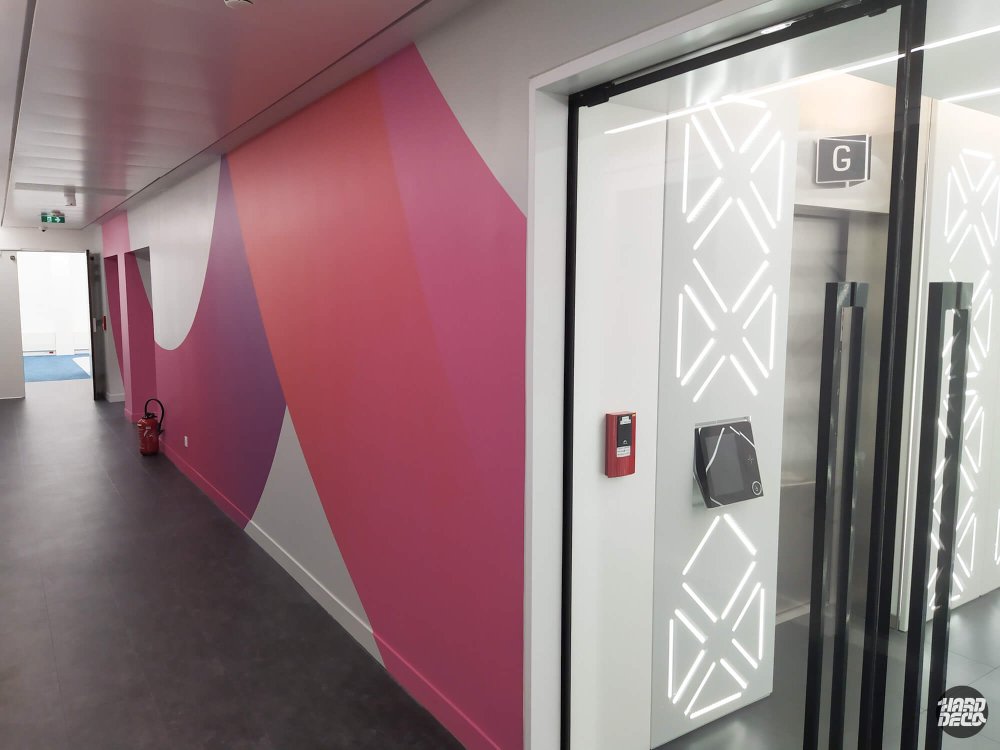 Décoration murale abstraite rose et violet au niveau des ascenseurs du siège TCS, motifs géométriques lumineux
