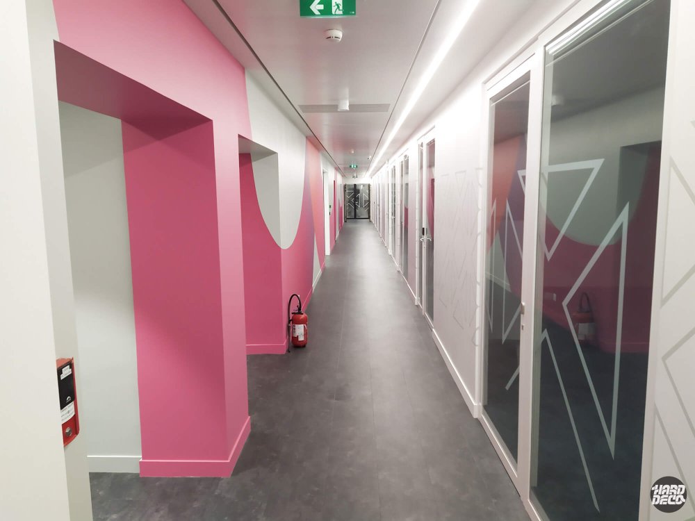 Vue d'ensemble du couloir TCS peint en rose fuchsia avec formes organiques abstraites et vitrages géométriques