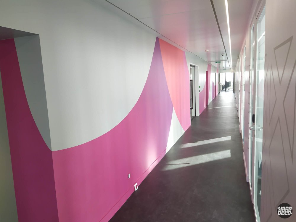 Couloir bureaux TCS avec composition abstraite rose poudré et fuchsia sur mur long, lumière naturelle
