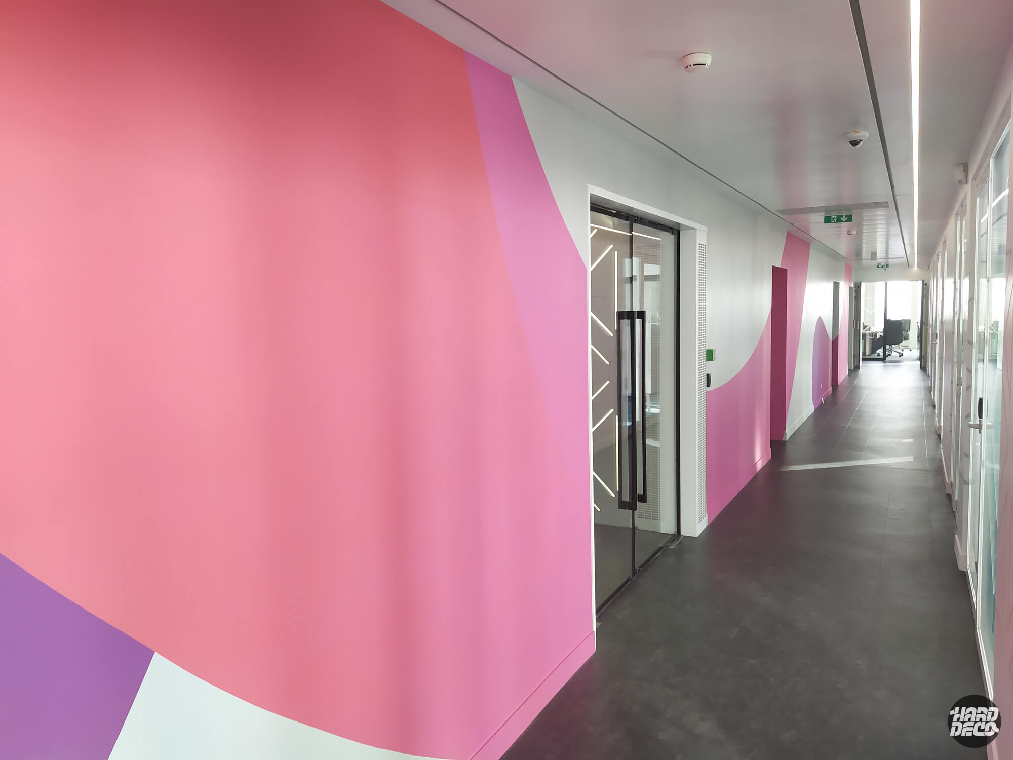Couloir de bureaux TCS décoré de grandes formes abstraites roses et mauves sur mur, vue en perspective