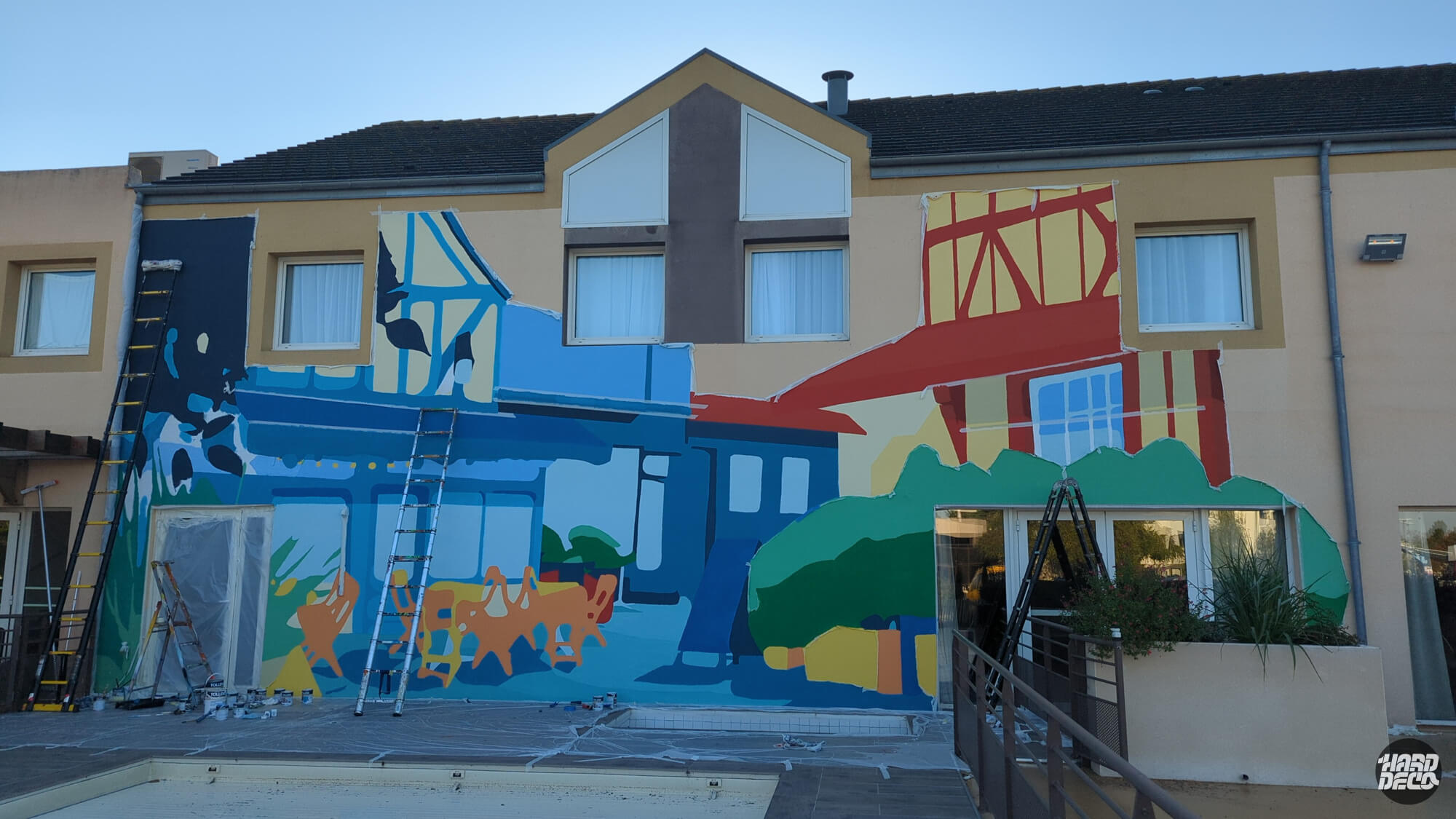 Fresque murale en cours de réalisation sur façade hôtel à Caen, colombages et terrasse normande colorée