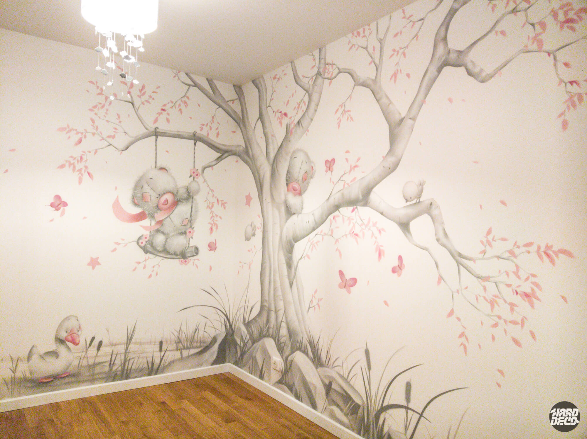 Fresque murale chambre bébé : ourson sur balançoire, arbre gris et papillons rose, angle de la pièce