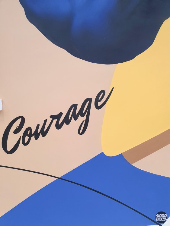 Détail fresque murale judo Combs-la-Ville, mot Courage en cursive noire sur fond sable avec formes bleu marine et jaune