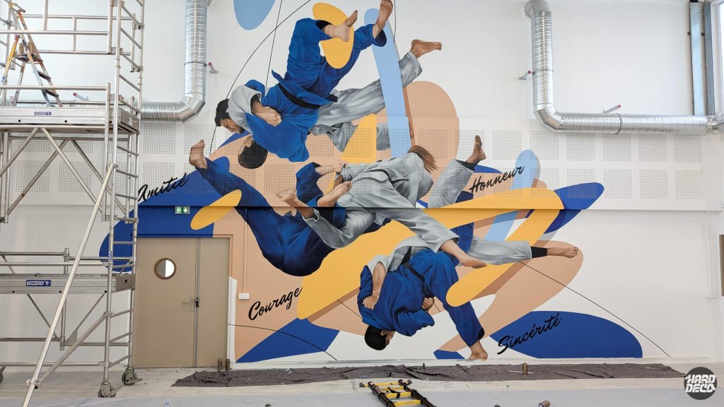 Réalisation fresque murale judo Combs-la-Ville en cours, échafaudage visible, judokas projetés sur fond doré et bleu