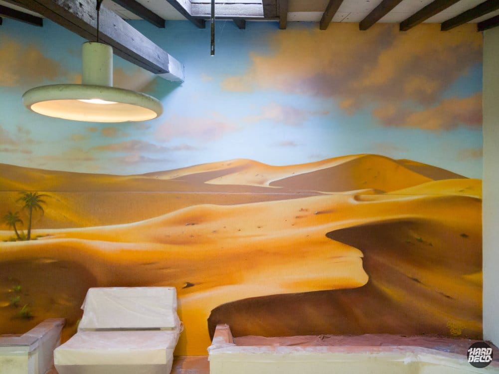 Fresque murale dunes désert aérosol, dégradé ocre sous ciel nuageux, gros plan sur composition