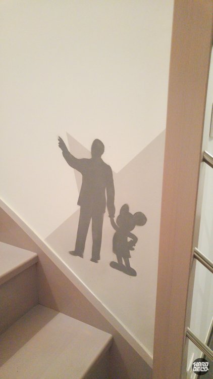 Silhouette grise de Walt Disney tenant Mickey Mouse par la main, peinte sur mur d'escalier en angle