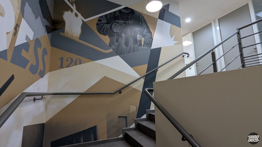 Détail fresque Express escalier, technicien en grisaille et chiffre 120 sur fond géométrique beige