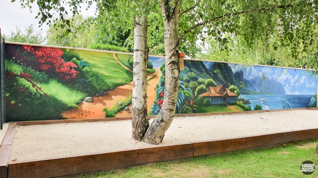 Vue large fresque extérieure paysage polynésien sur clôture, boulodrome et arbres au premier plan