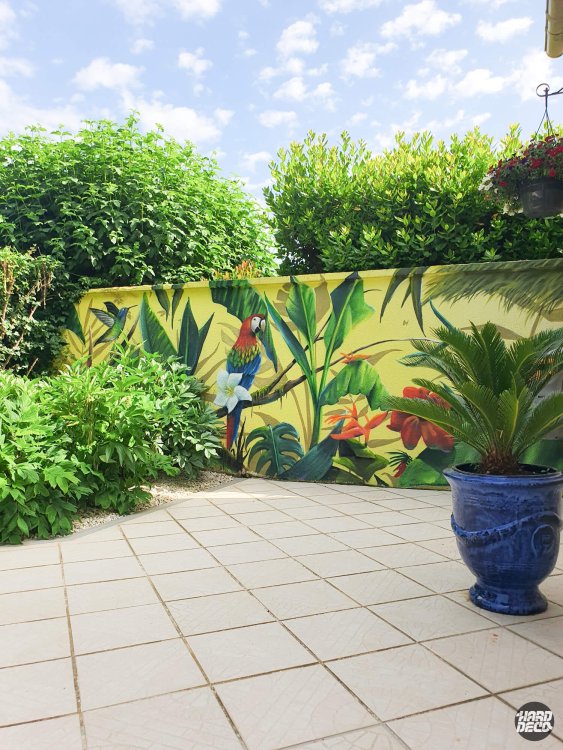 Fresque murale tropicale extérieure avec ara écarlate, feuilles de bananier et fleurs exotiques sur fond jaune