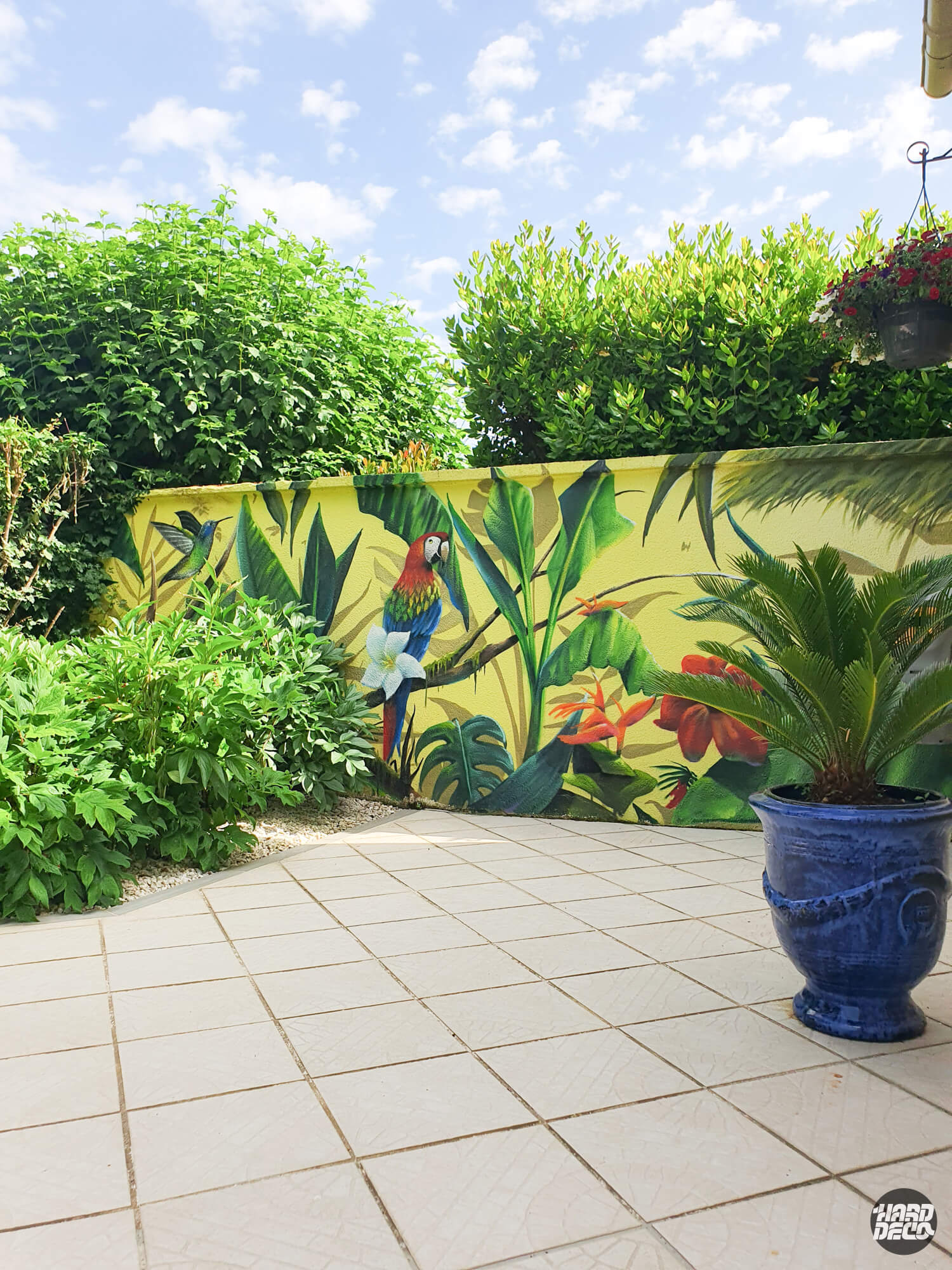 Fresque murale tropicale extérieure avec ara écarlate, feuilles de bananier et fleurs exotiques sur fond jaune