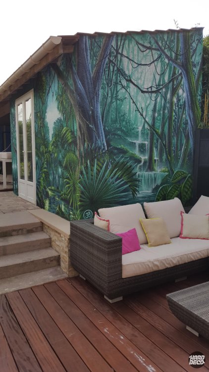 Fresque murale jungle avec cascade centrale sur façade extérieure, terrasse bois et salon de jardin