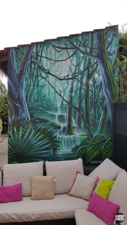 Détail fresque jungle cascade aérosol sur façade, troncs bleutés et feuillage vert profond, signature Star97