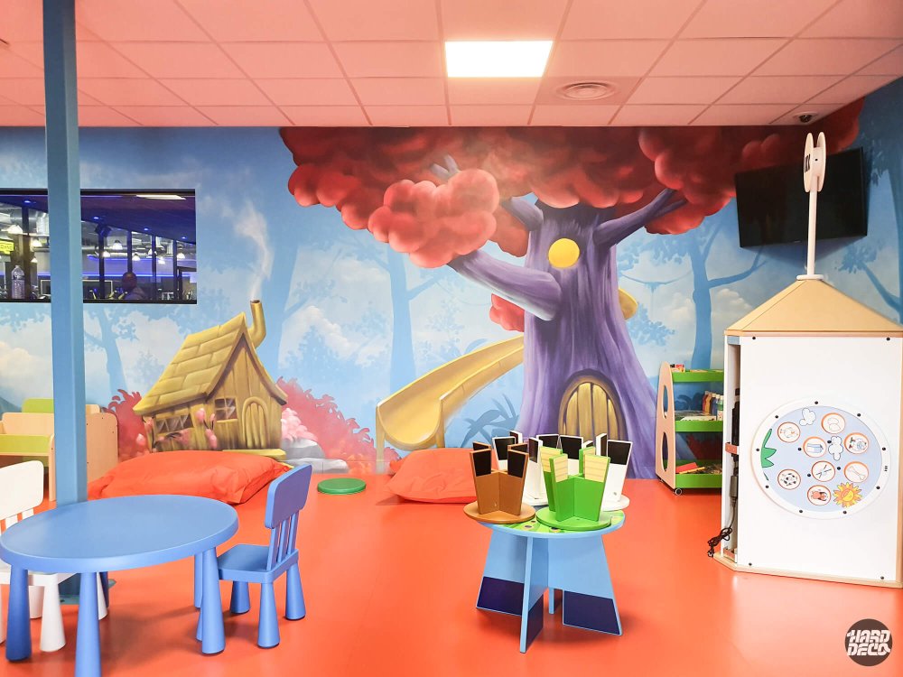Salle de jeux enfant Fitness Park avec fresque forêt enchantée, arbre habité et toboggan peints sur mur bleu