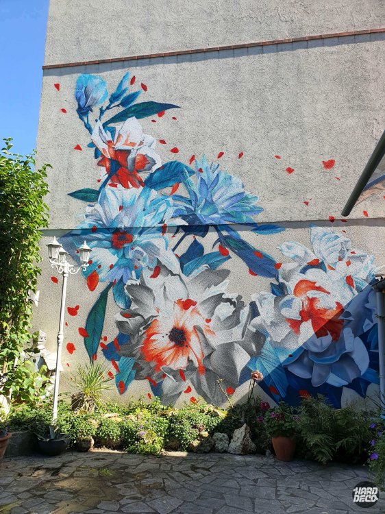 Fresque florale extérieure aérosol, pivoines bleues et grises avec pétales orange sur façade enduite, vue rapprochée jardin