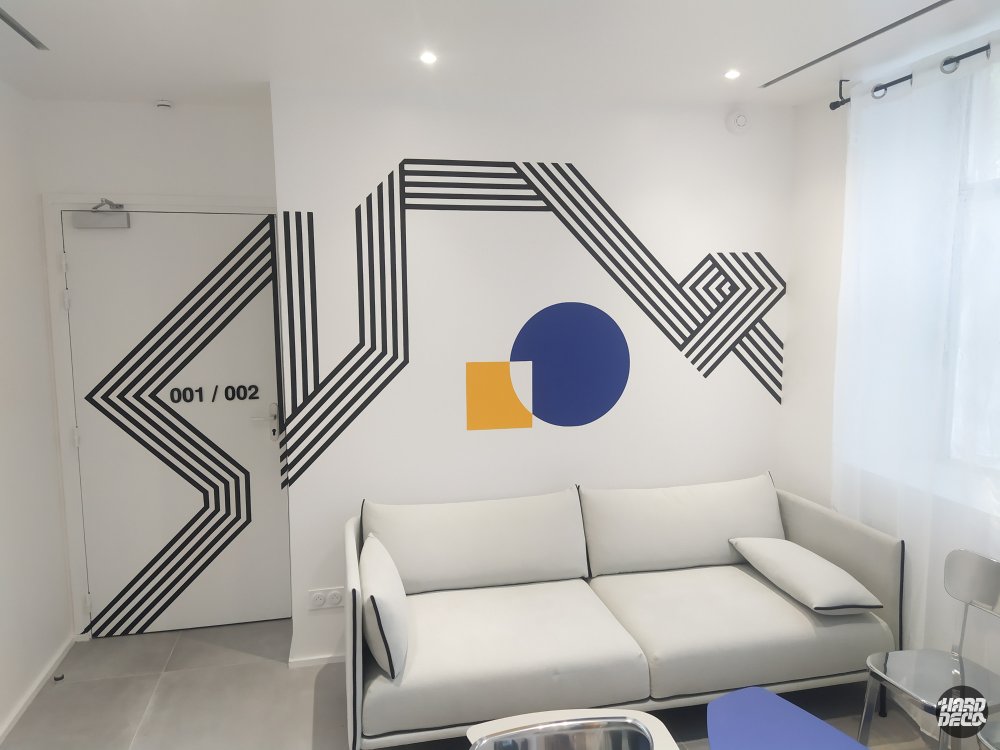 Fresque géométrique noire et blanche avec cercle bleu et carré jaune, mur salon hôtel Graphik