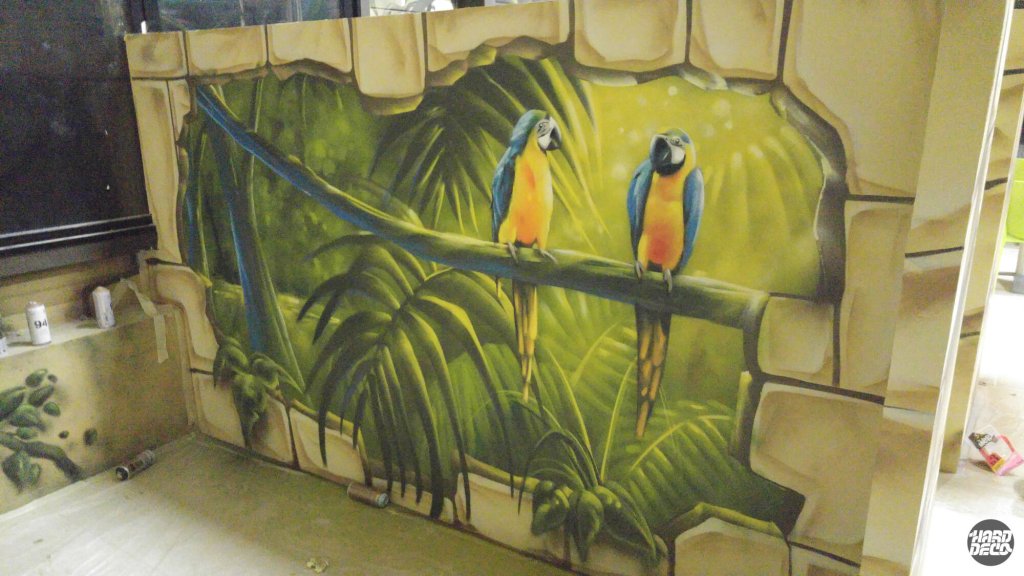 Deux aras bleus et jaunes sur branche devant feuillage tropical vert, fresque aérosol Wahoo Park Servon