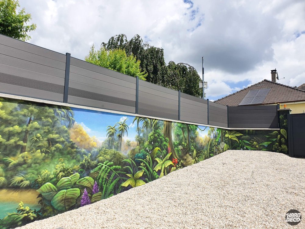 Fresque murale jungle tropicale sur clôture extérieure, végétation dense et ciel bleu, vue d'ensemble angle gauche