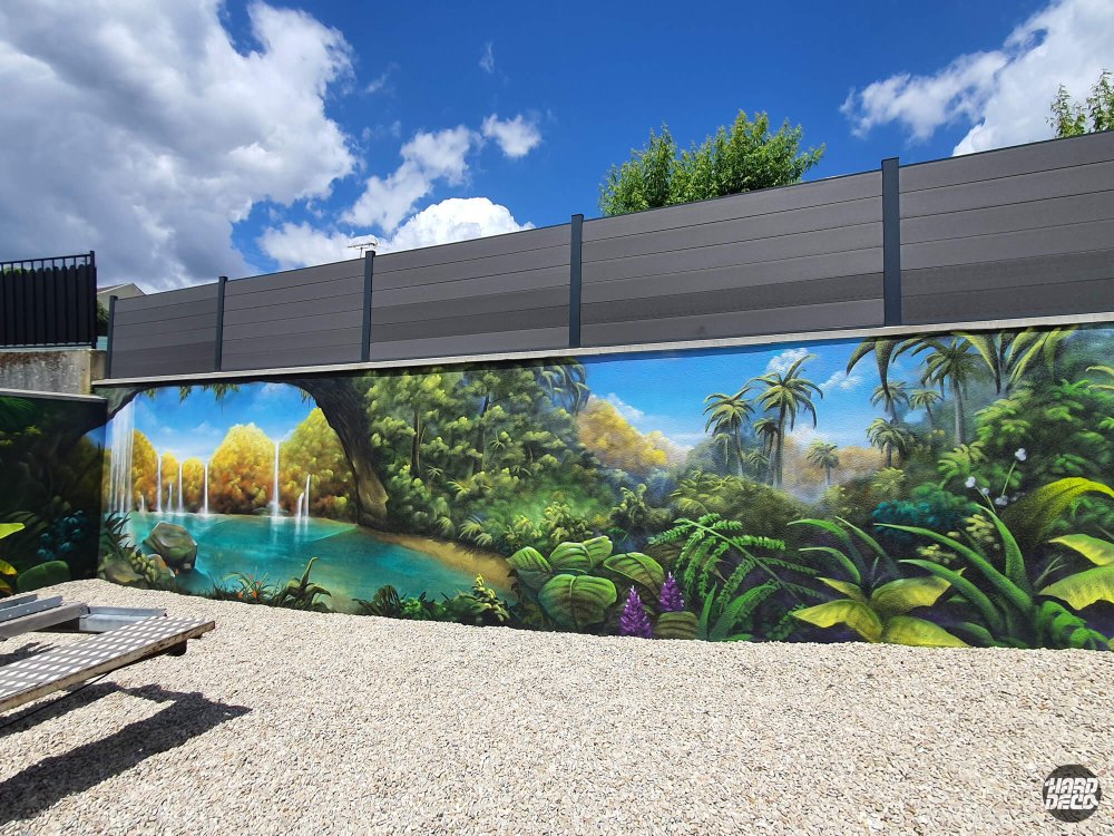 Fresque jungle tropicale sur clôture extérieure, lac turquoise et palmiers, lumière naturelle ciel bleu