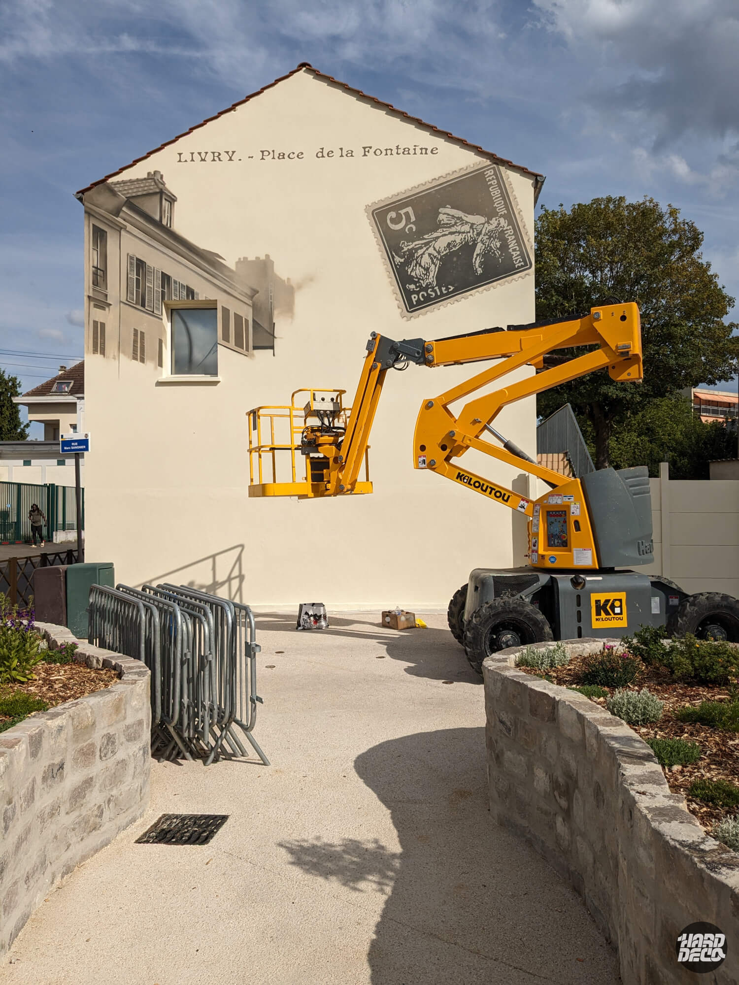Réalisation fresque façade Livry-Gargan en nacelle élévatrice Kiloutou, travail en hauteur sur pignon avec timbre postal en cours de peinture