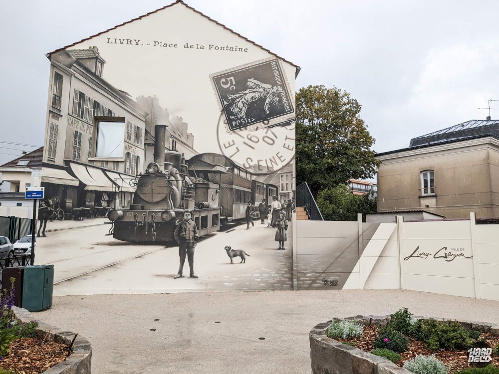 Fresque façade Livry-Gargan, reproduction carte postale ancienne Place de la Fontaine avec locomotive à vapeur EST 20 en sépia