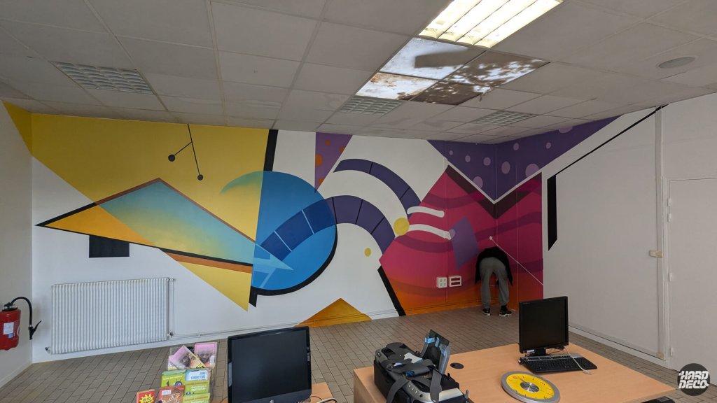 Peinture murale en cours de réalisation salle informatique Montfermeil, artiste au travail sur décor géométrique coloré