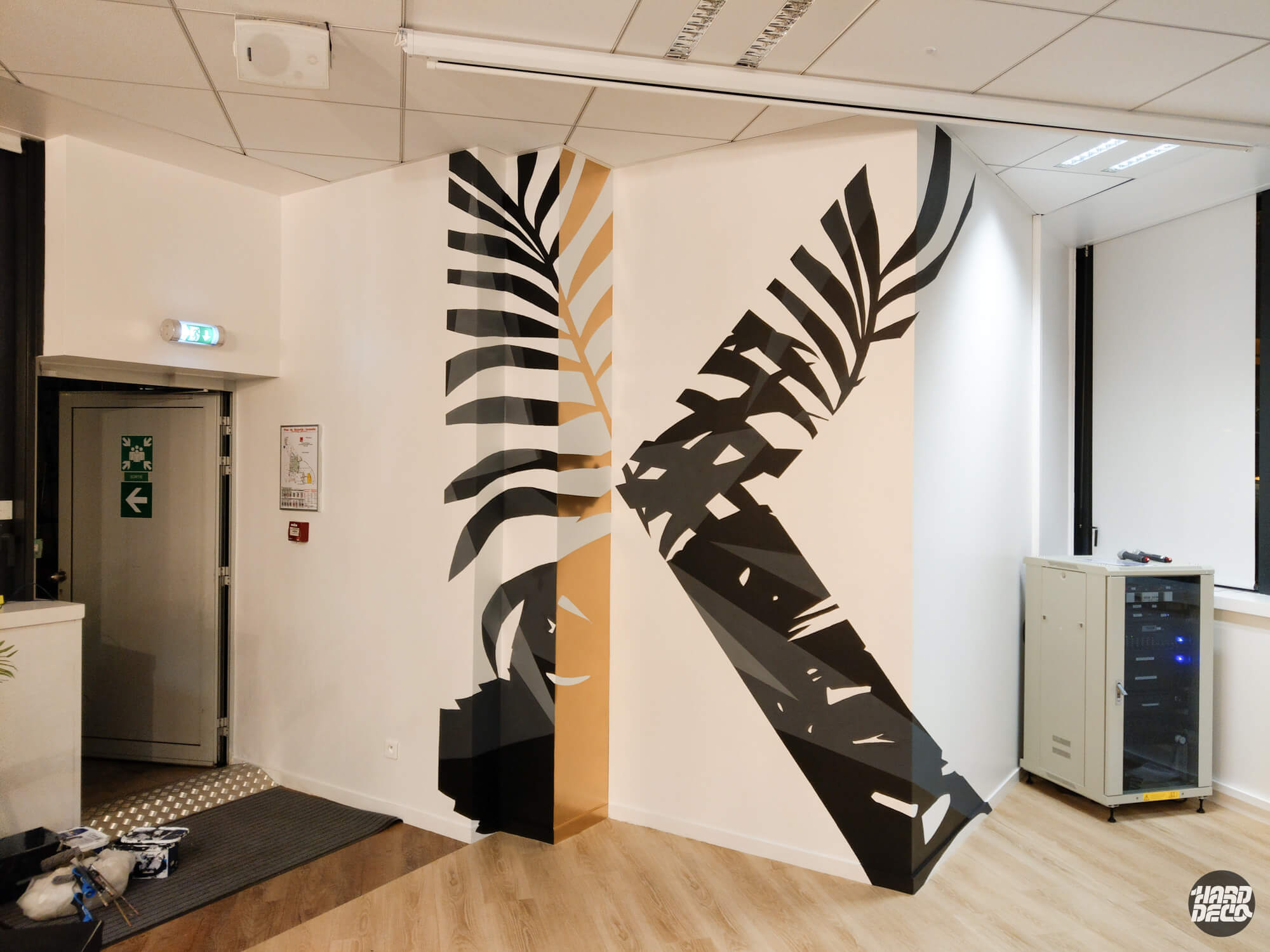 Fresque anamorphose feuilles tropicales noir et or sur angle de mur, bureaux Kantar Paris