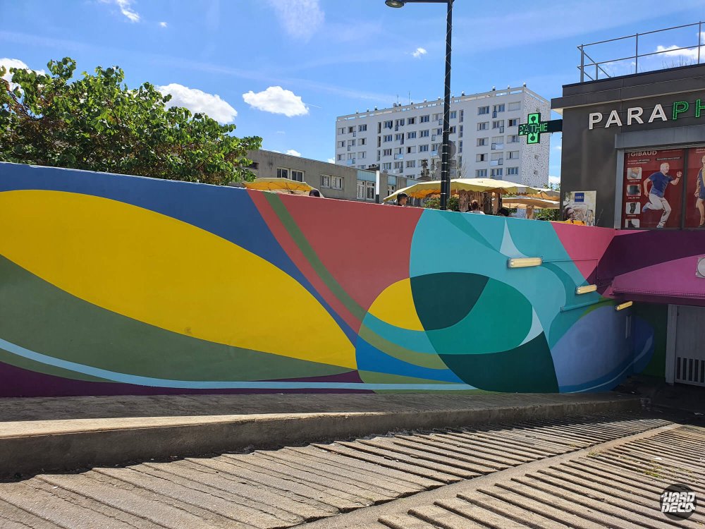 Fresque murale abstraite muret parking extérieur aplats courbes jaune teal rose ambiance lumière naturelle