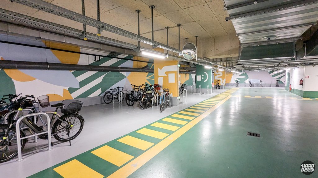Long couloir du parking vélos entièrement décoré de fresques murales abstraites jaune et vert, Paris 19e