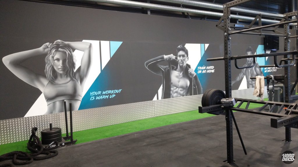 Mur complet fresque Fitness Park Pierrefitte, trois personnages sportifs en gris et bleu, vue depuis la zone de musculation