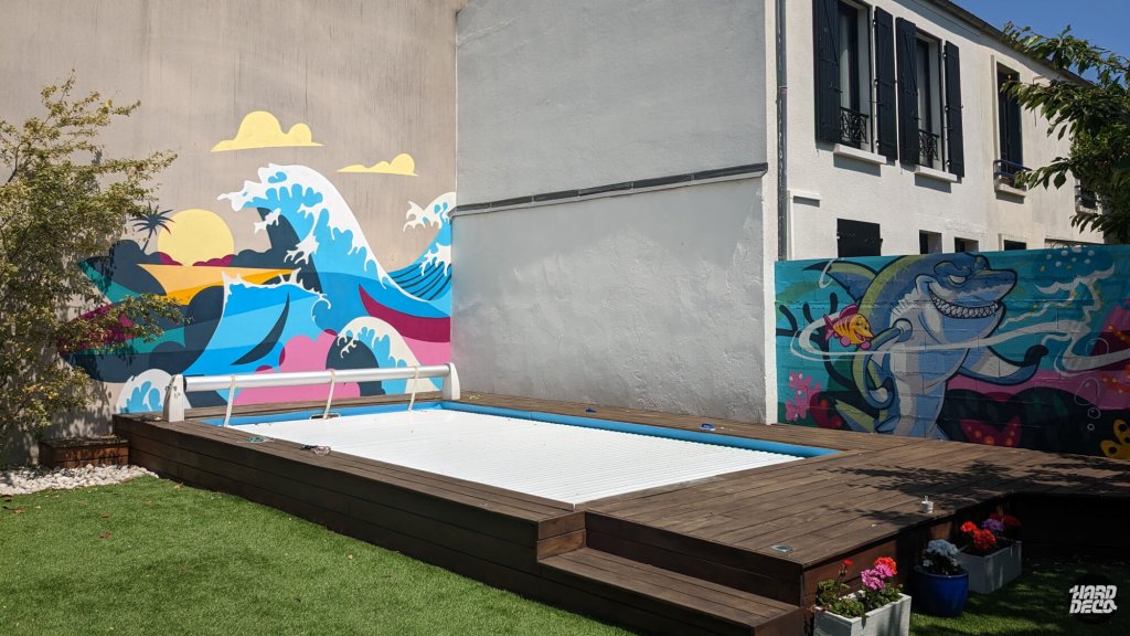 Vue d'ensemble complète piscine jardin avec fresque vague soleil couchant et requin cartoon aérosol