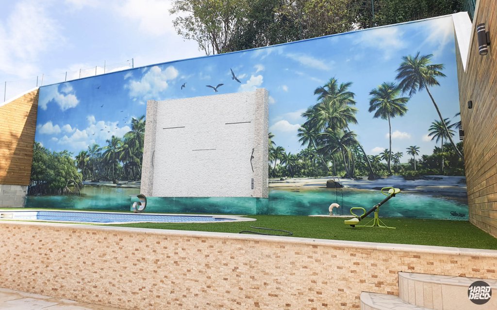 Fresque aérosol extérieure 70 m² plage et cocotiers sur mur de piscine, vue légèrement latérale