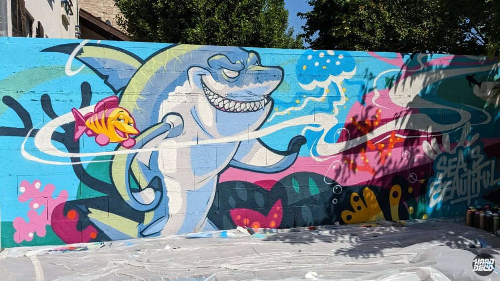 Fresque aérosol requin cartoon et poisson orange sur mur extérieur, univers sous-marin coloré