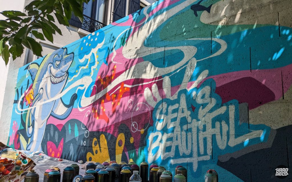 Vue en angle de la fresque requin avec inscription Sea is Beautiful, bombes de peinture au sol