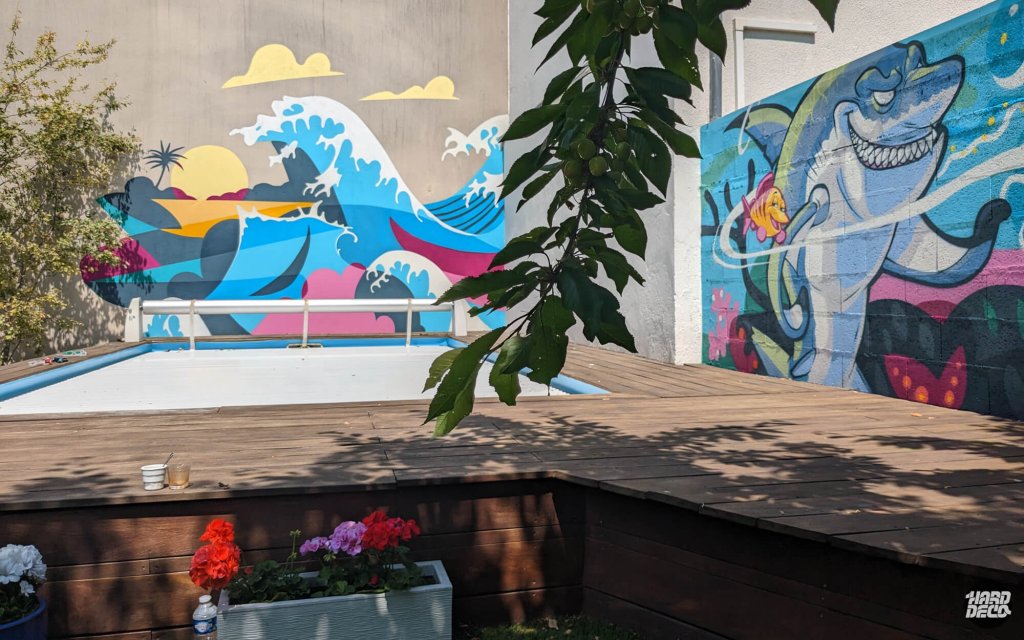 Terrasse piscine avec fresque vague Hokusai et requin street art, géraniums au premier plan