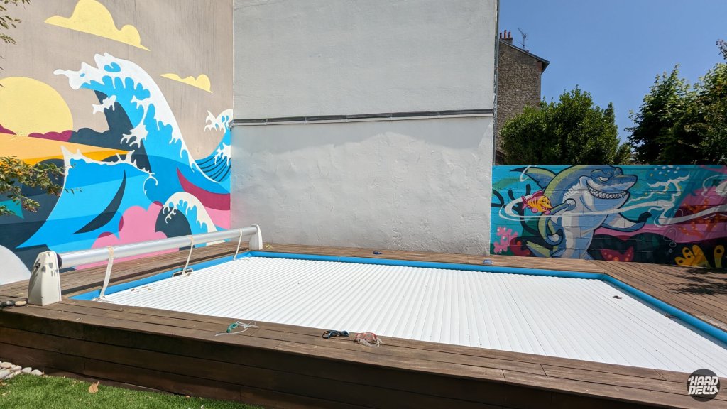 Piscine couverte entourée des deux fresques murales vague et requin, ciel bleu et verdure