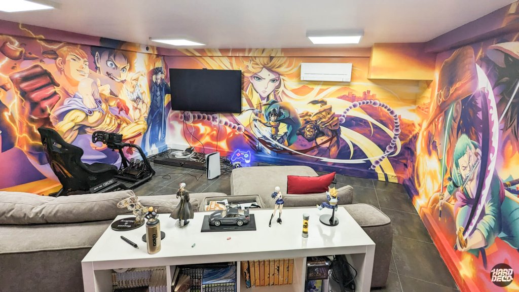 Vue panoramique salle gaming fresque manga 360°, simulateur de conduite et figurines au premier plan
